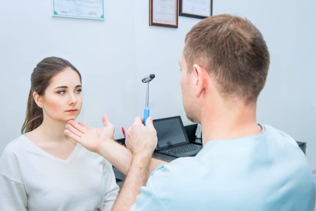 neurologist doctor inspecting young female patient's nervous system using a hammer.